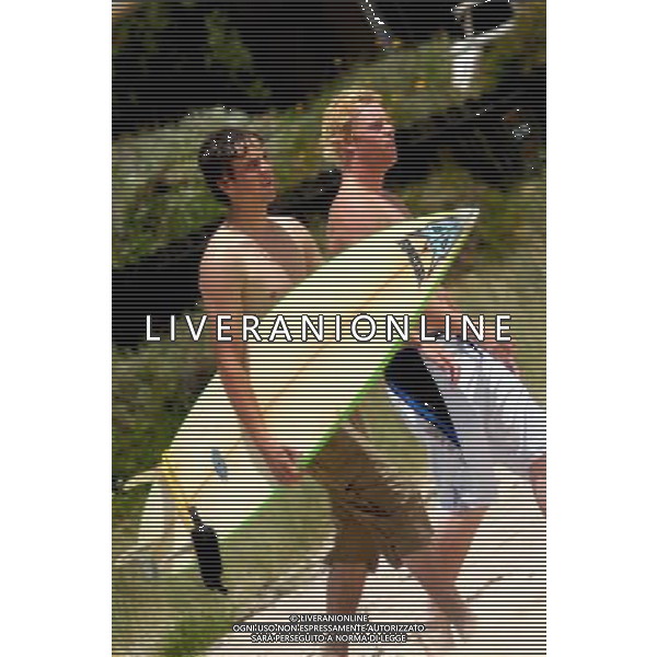 NZ surfers walking with surfing board on a beach.