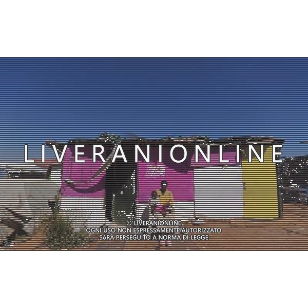 (110831) -- JOHANNESBURG, Aug. 31, 2011 () -- Nemukula Shonisayi carries her child Amkuniselo Nemukula in front of her sheet iron house at the Ramseg Informal settlement in Johannesburg, South Africa, Aug. 24, 2011. One of the most common landscapes in Johannesburg and even the whole South Africa is slum, some of which stretche for miles and are populated with hundreds and thousands of people. For most of the inhabitants, their houses are made from scrap materials such as wooden stakes or corrugated metal. Although living in a shanty town, poverty cannot stop their pursuit for beauty, nor ruin their impulse in life. Therefore, they find a way to express their love for life, to painting on the iron sheet house.(/Fei Maohua) (msq)
